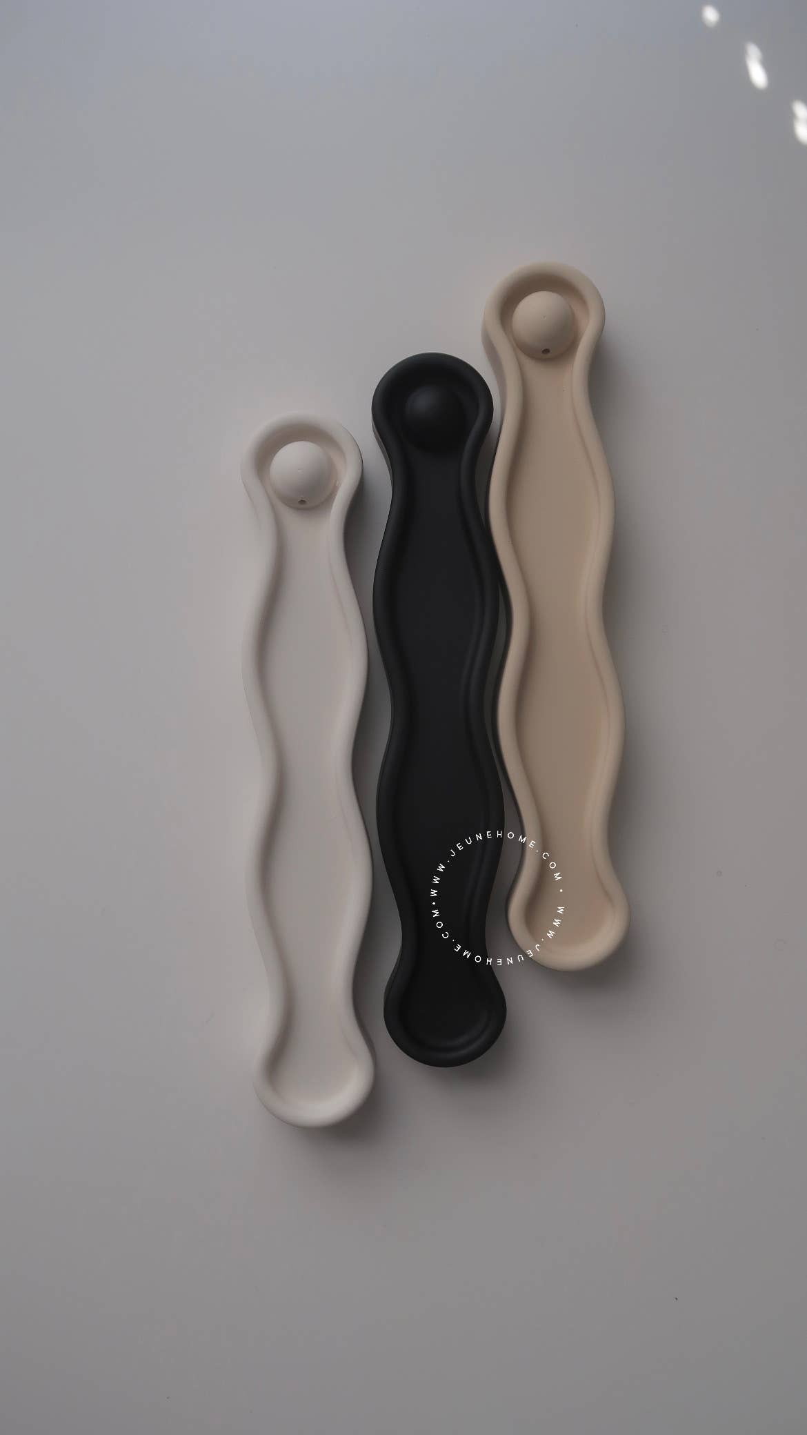 Three wavy-shaped objects in beige, black, and beige on a light gray background